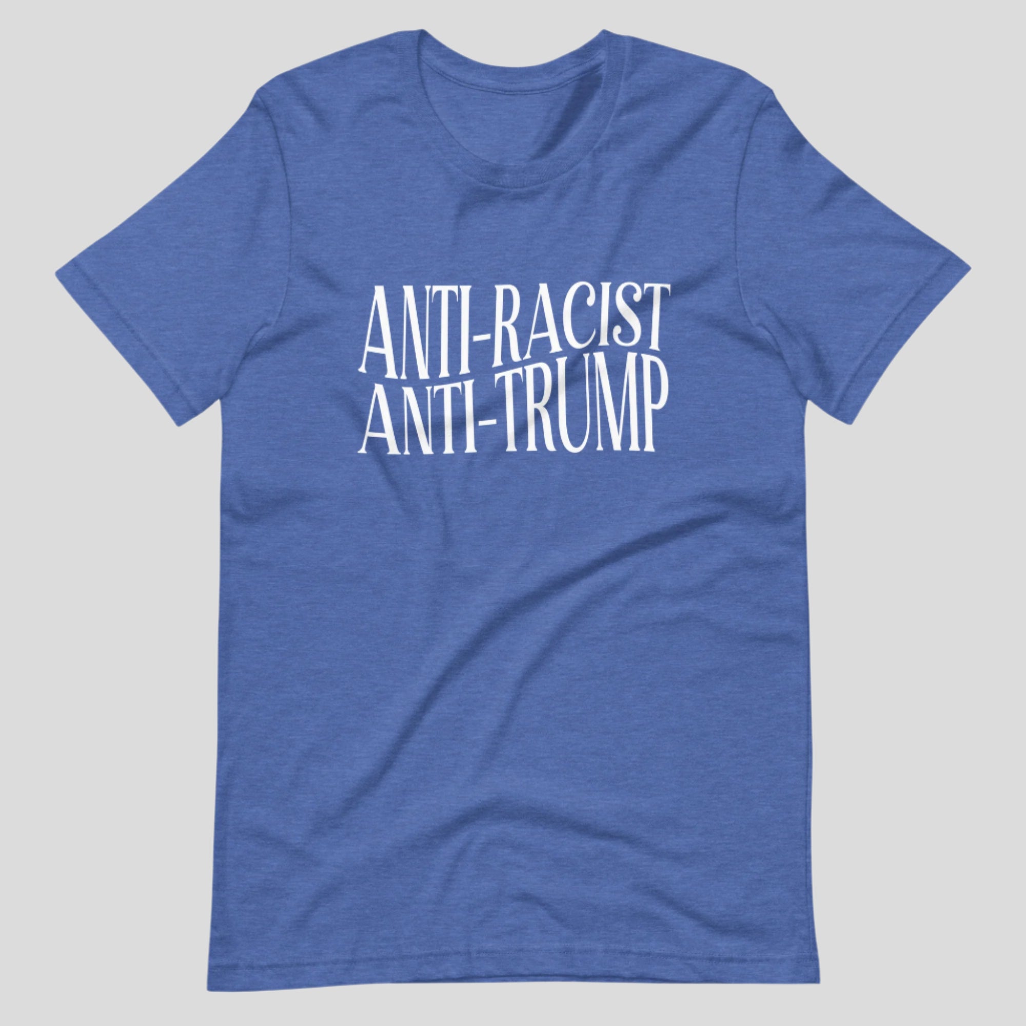 Flat lay of a blue heather t-shirt on a neutral background. The shirt features white serif text across the chest that reads: “Anti-Racist Anti-Trump.”