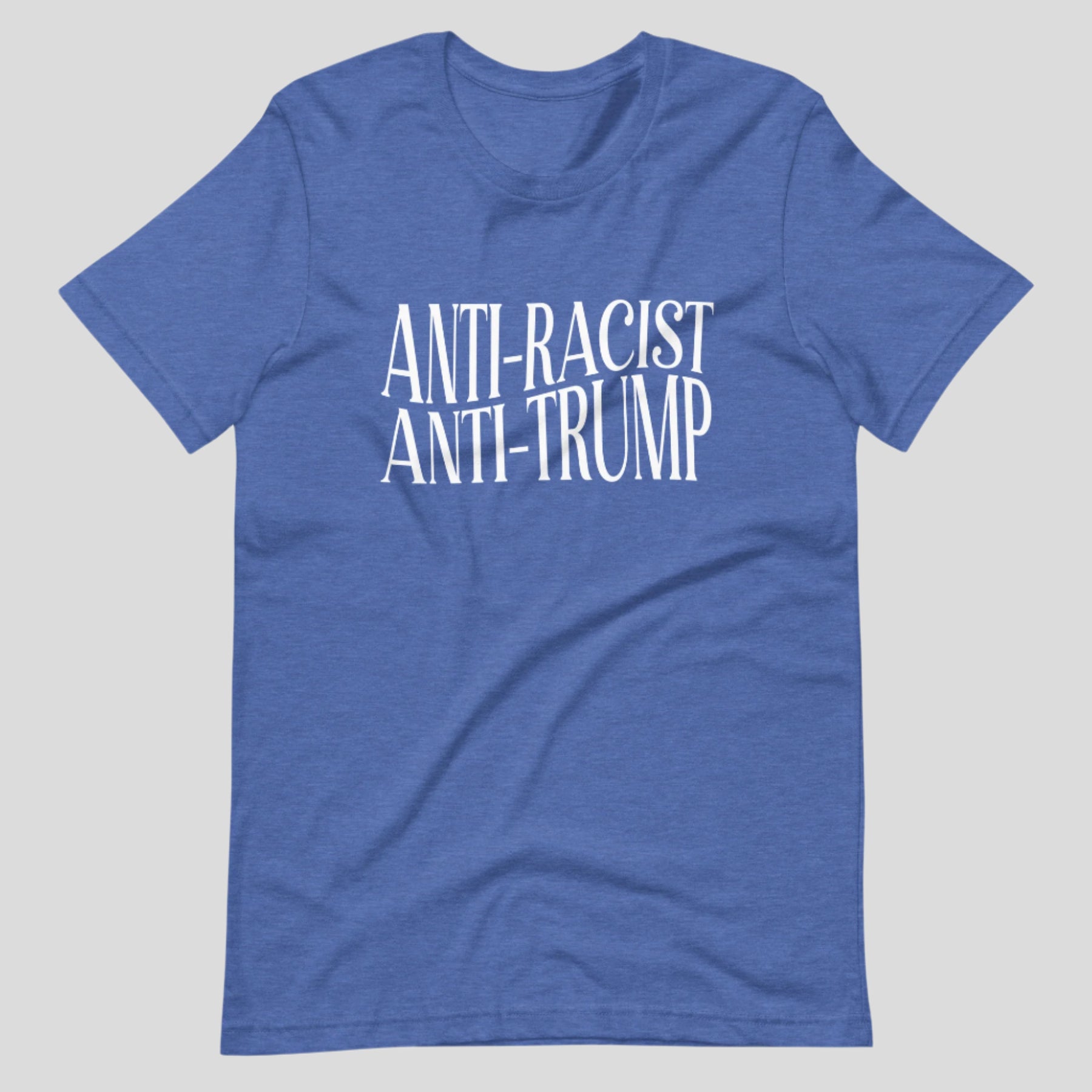 Flat lay of a blue heather t-shirt on a neutral background. The shirt features white serif text across the chest that reads: “Anti-Racist Anti-Trump.”
