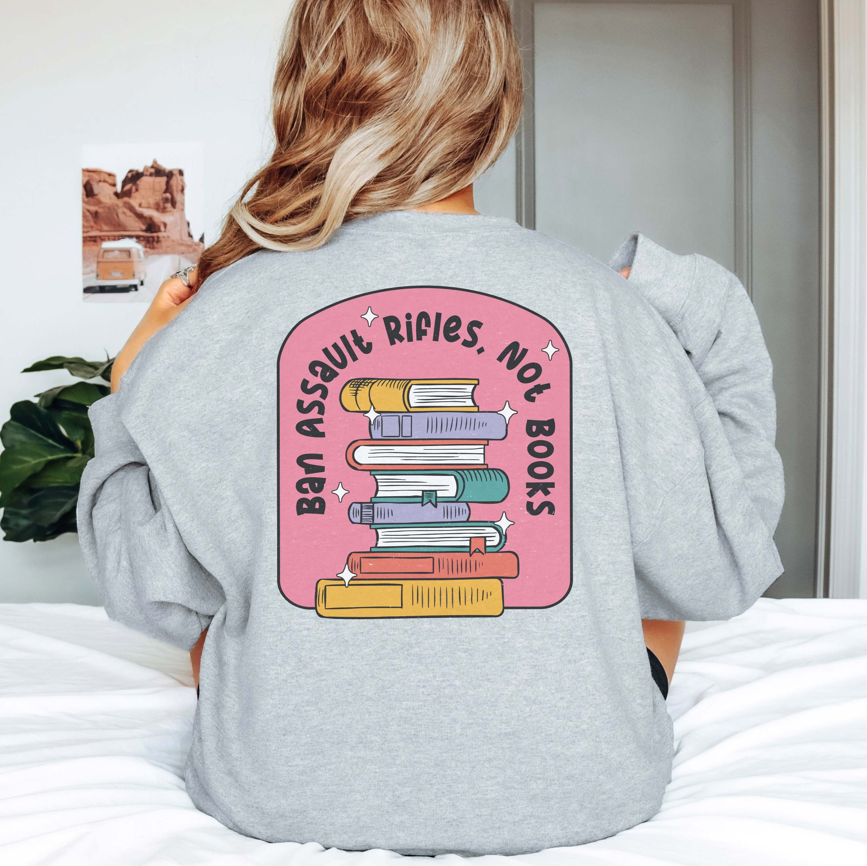 Back view of a woman wearing a grey sweatshirt with the words 'Ban Assault Rifles Not Books' printed on the back.