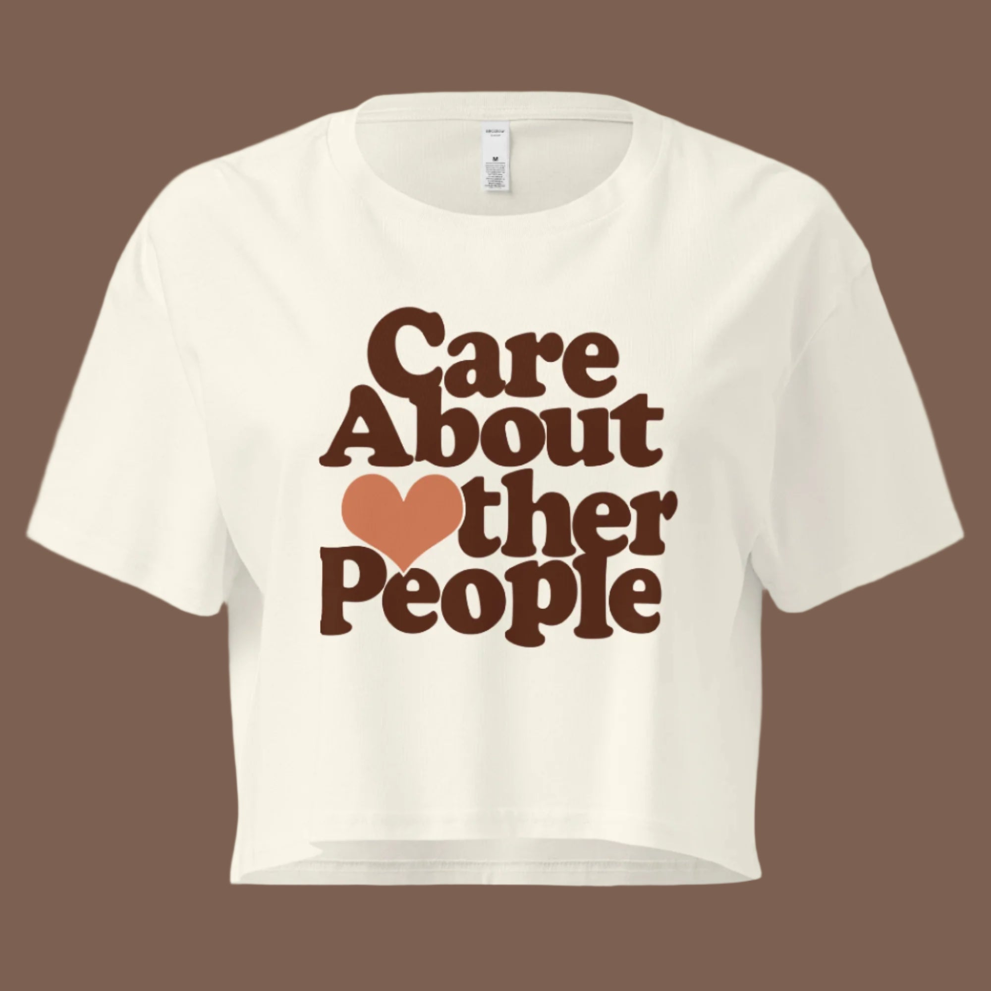 Flat lay of a natural-colored women’s crop top with bold dark brown text reading “Care About Other People.” The "O" in "Other" is replaced with a small orange heart. The shirt has a relaxed fit, dropped shoulders, and a cropped length, displayed on a neutral background with a clean, modern aesthetic.