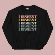 Flat lay of a black crewneck sweatshirt on a pink background. The sweatshirt features the phrase “I dissent” repeated multiple times across the front in bold, multicolored text.