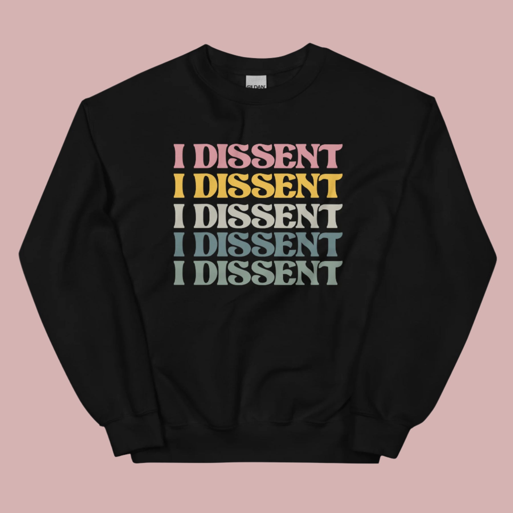 Flat lay of a black crewneck sweatshirt on a pink background. The sweatshirt features the phrase “I dissent” repeated multiple times across the front in bold, multicolored text.