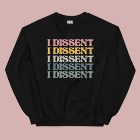 Flat lay of a black crewneck sweatshirt on a pink background. The sweatshirt features the phrase “I dissent” repeated multiple times across the front in bold, multicolored text.