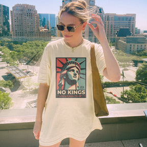 Person wearing a t-shirt with a graphic design of the Statue of Liberty and 'No Kings' Liberty and Justice for all text standing in an urban setting.