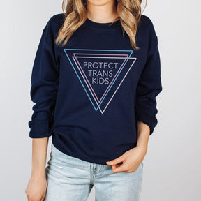 Woman wearing a navy blue sweatshirt that says 'Protect Trans Kids' with three triangles in blue, pink, and white representing the transgender flag.