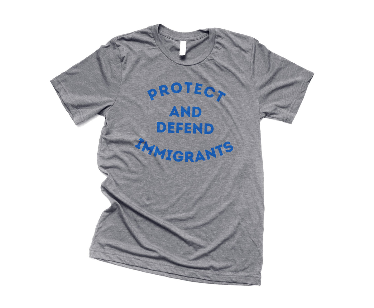 Gray t-shirt with blue text 'PROTECT AND DEFEND IMMIGRANTS' on a white background